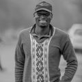 Black and white portrait of a smiling man in a patterned sweater outdoors.