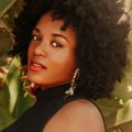 Cheerful young African American female with afro hairstyle and earrings looking at camera